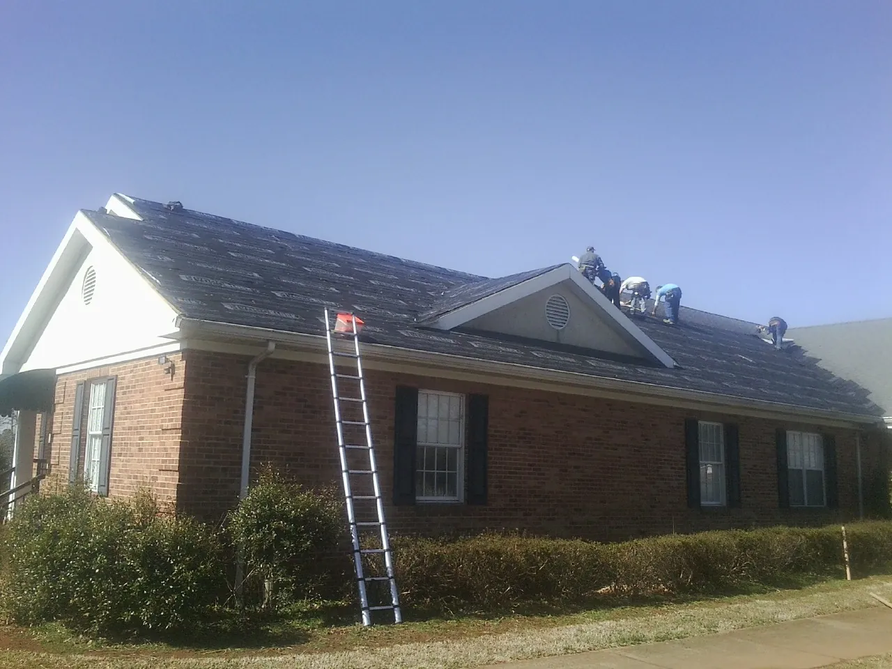 Crew tearing shingles off a brick ranch roof with a ladder set — Emergency Roof Repair work by our crew in Stanton
