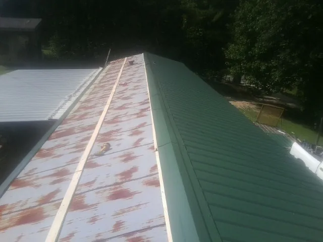 Old rusted panels beside newly installed green metal roofing — Wind Damage Roof Repair by Roofing Brothers in Stanton