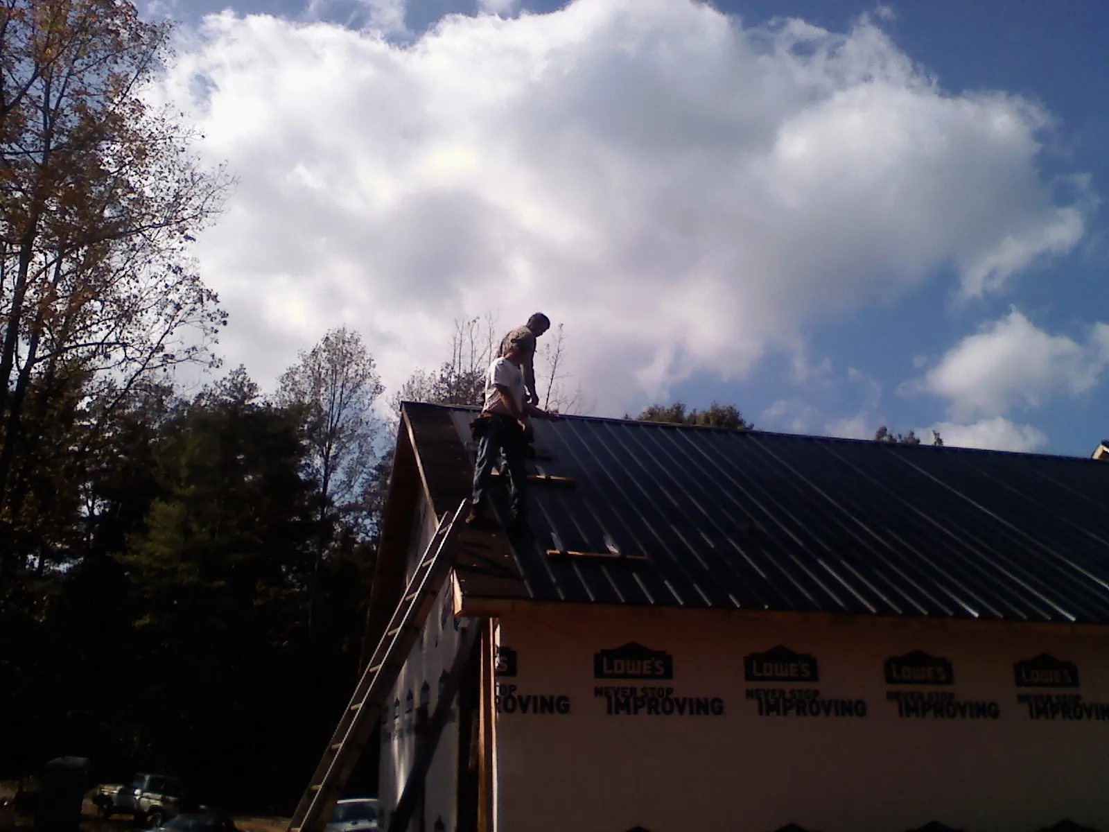 Roofer fastening dark metal panels high against a cloudy sky, from a Roof Inspection job in Stanton